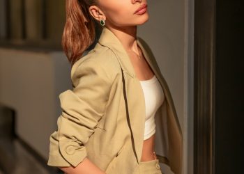 A woman in a tan suit leaning against a wall