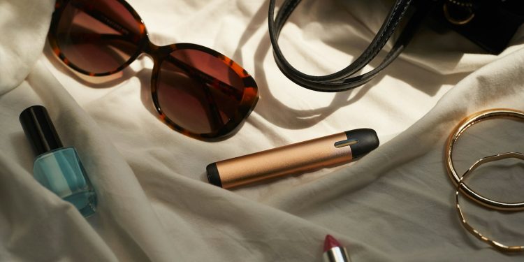 a pair of sunglasses, lipstick, and a purse on a bed